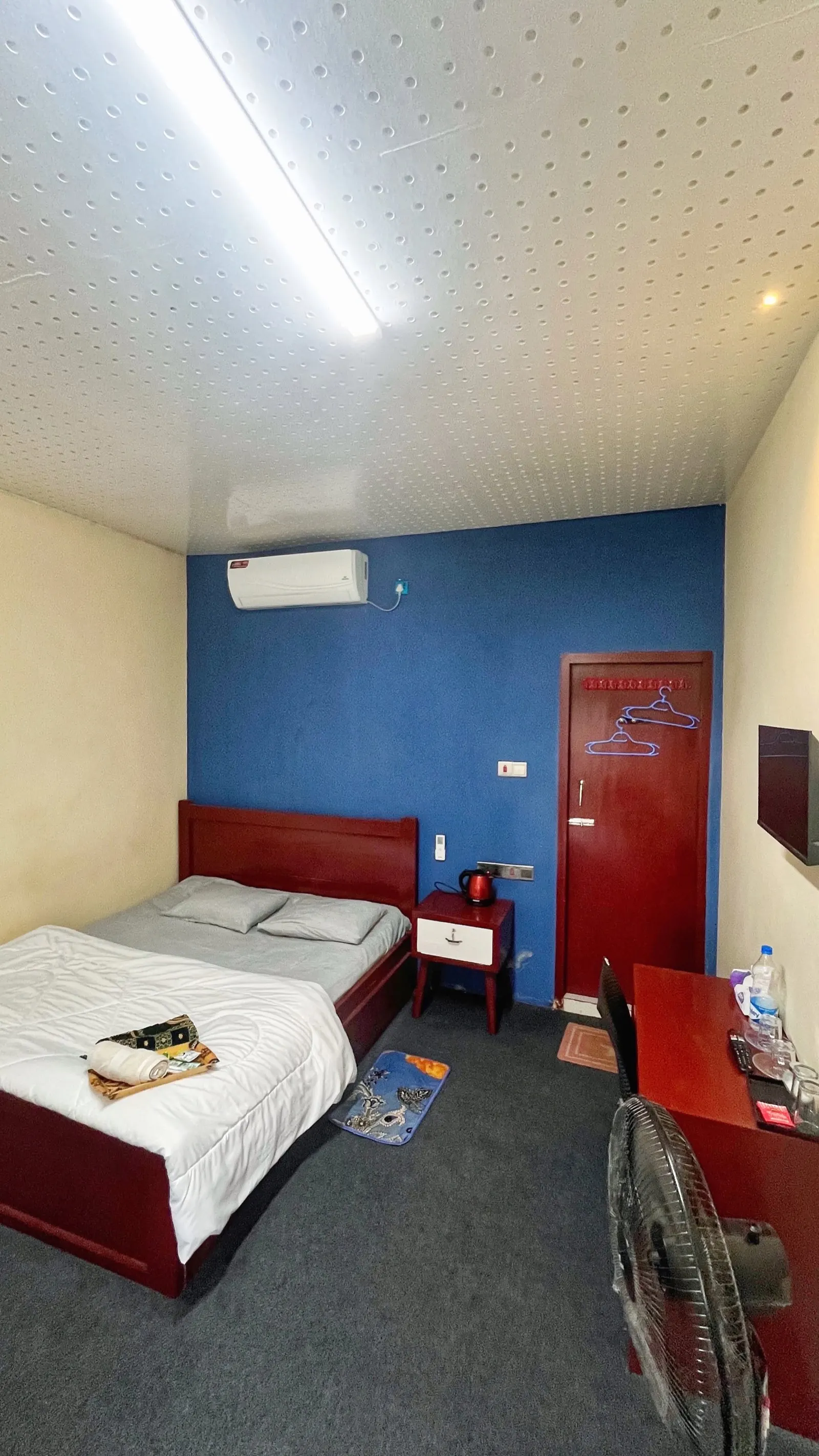 A guest room with a blue feature wall, air conditioning and a desk